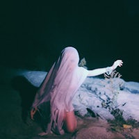 a woman in a white cloak kneeling on a rock at night